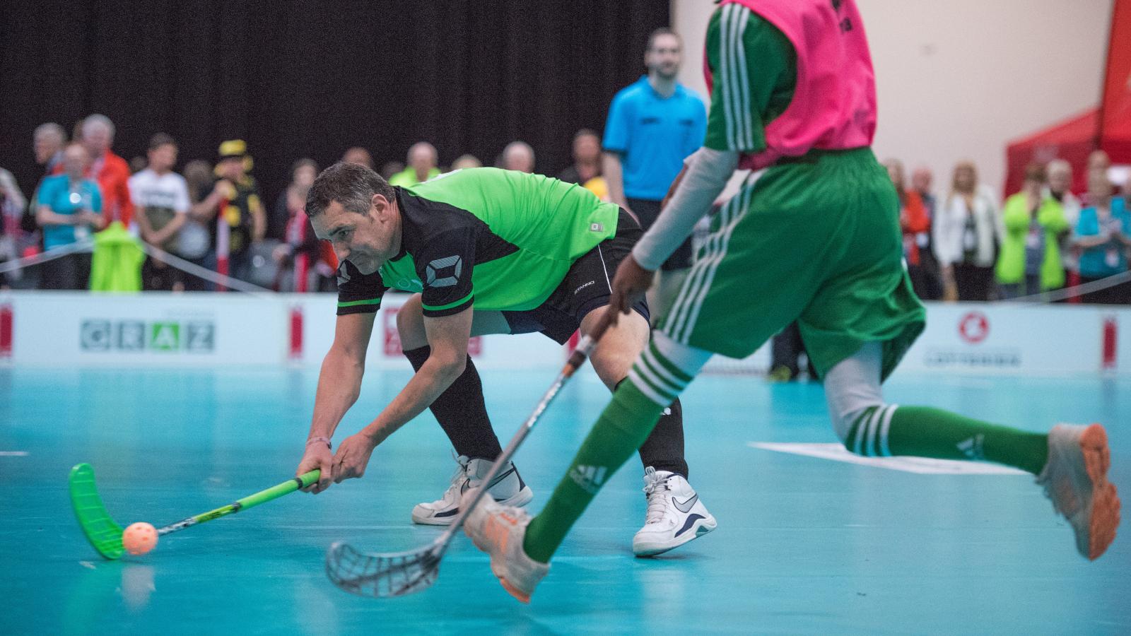 Floorball player striking ball past opponent with audience in background